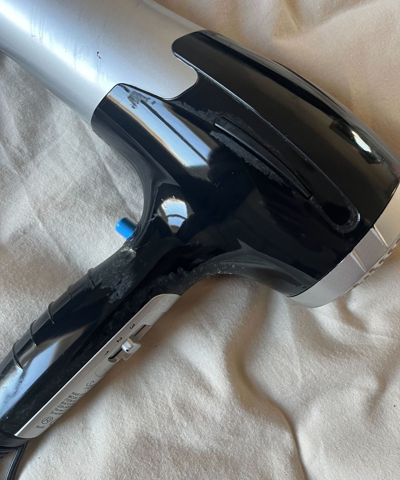 The shiny black handle of a hair dyer laying on cream bedding