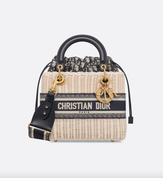 a wicker lady dior bag in front of a plain backdrop