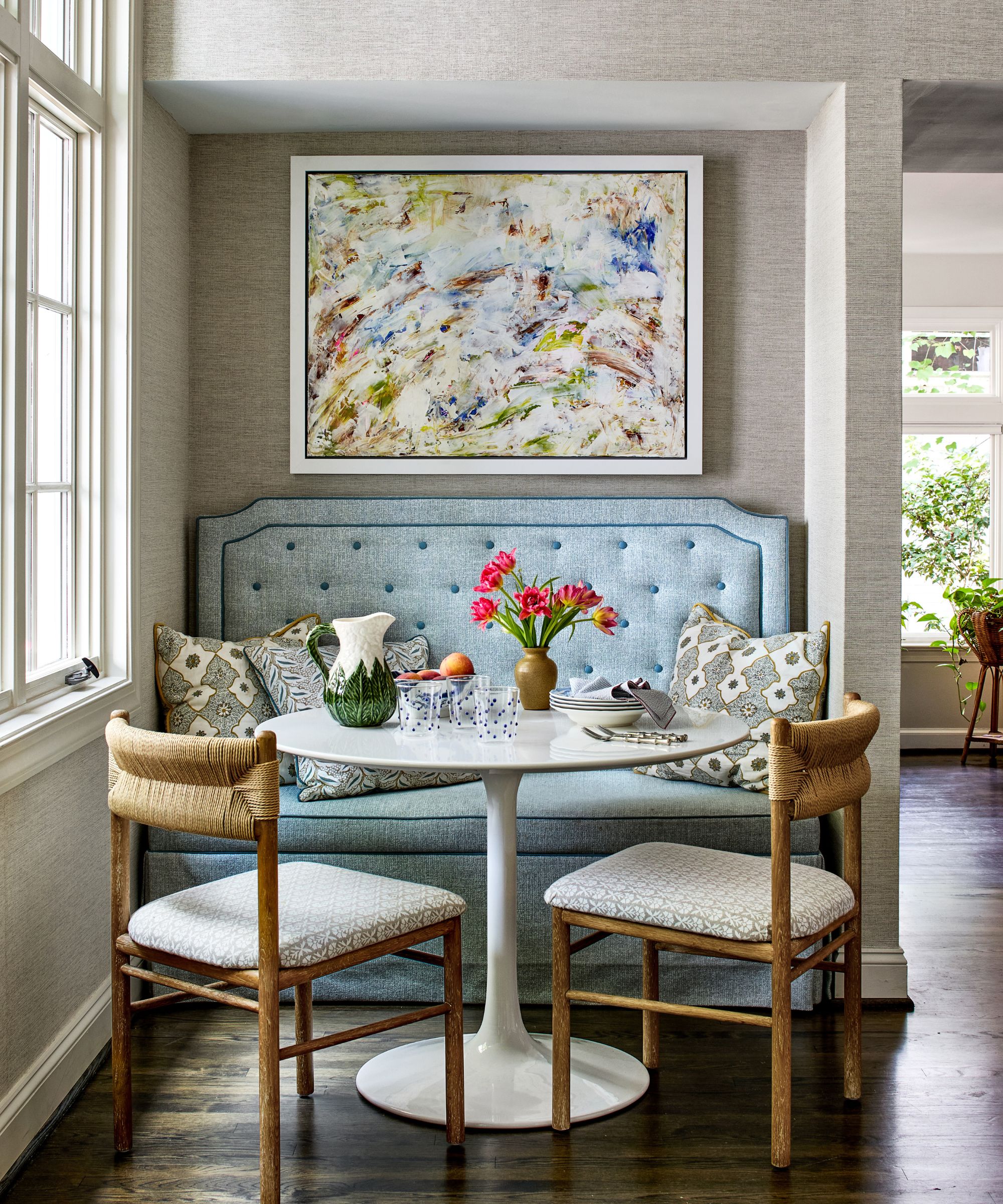 A small kitchen eat-in area with a blue banquette, a round white table, and two wooden dining chairs