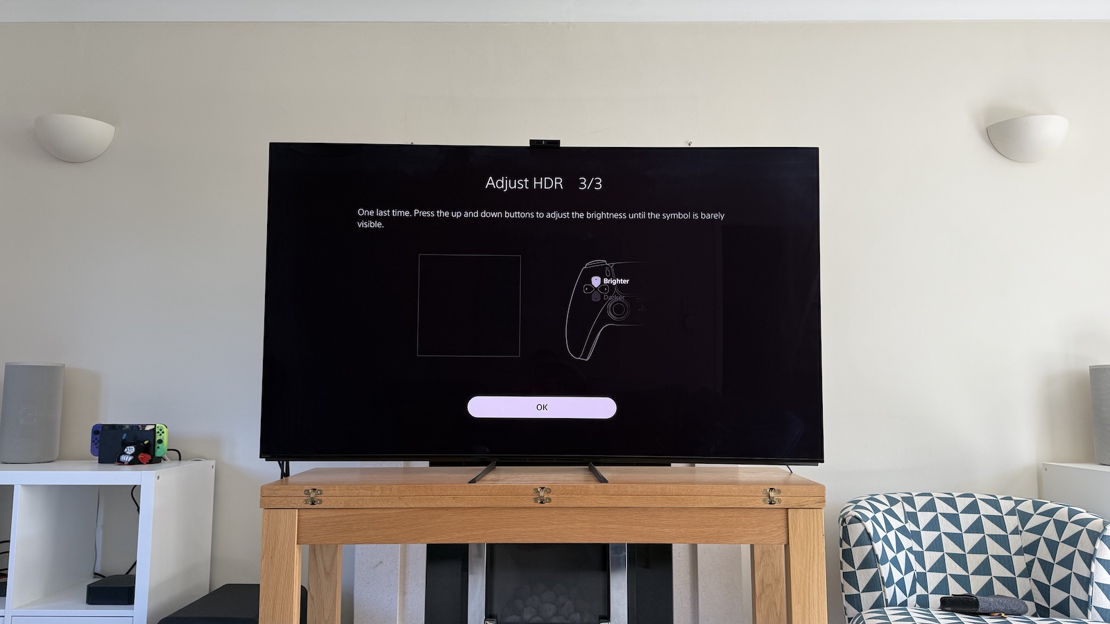 The 65-inch Sony A95L pictured on a wooden table in a living room. On the screen is the PS5 Adjust HDR menus