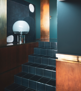 a teal tiled staircase with brass and wood materials surrounding it