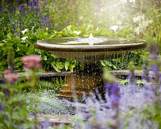 large water fountain in garden surrounded by purple flowers