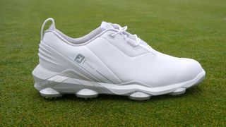 FootJoy Tour Alpha Shoe lying on the ground showing off its cleated design and cool white colorway