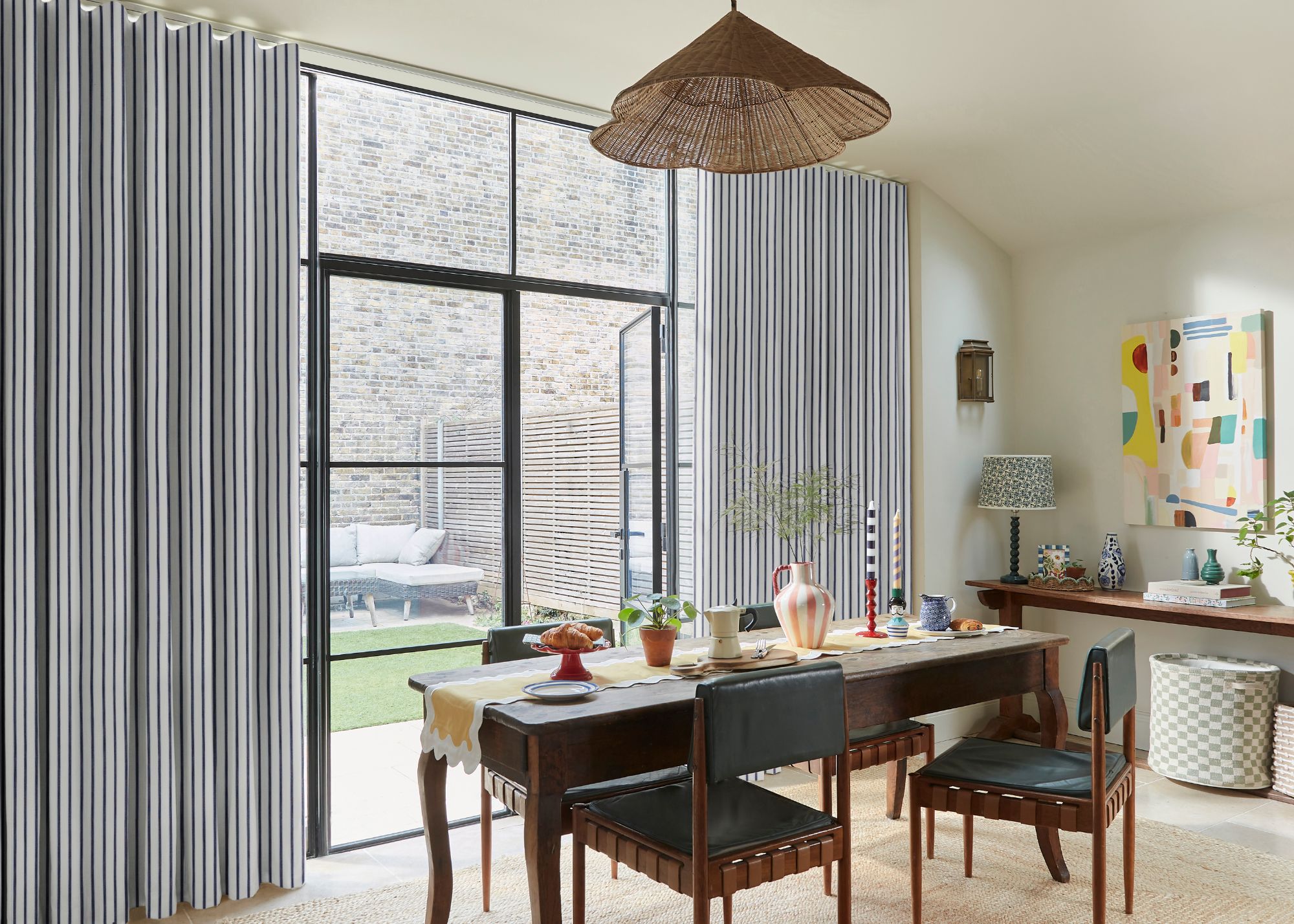 A modern dining room with striped wave curtains on glass doors leading to the garden.