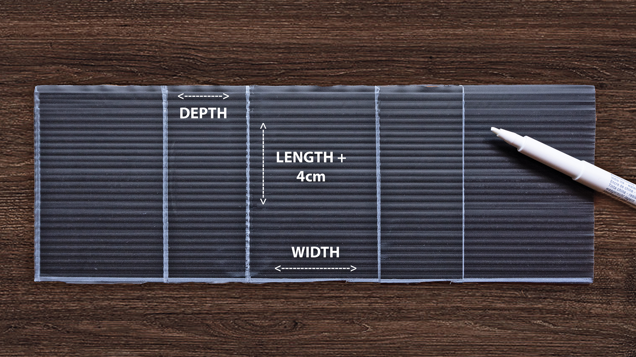 A clear plastic sheet on a wooden surface labeled with "Depth," "Length + 4cm," and "Width," with a white marker beside it