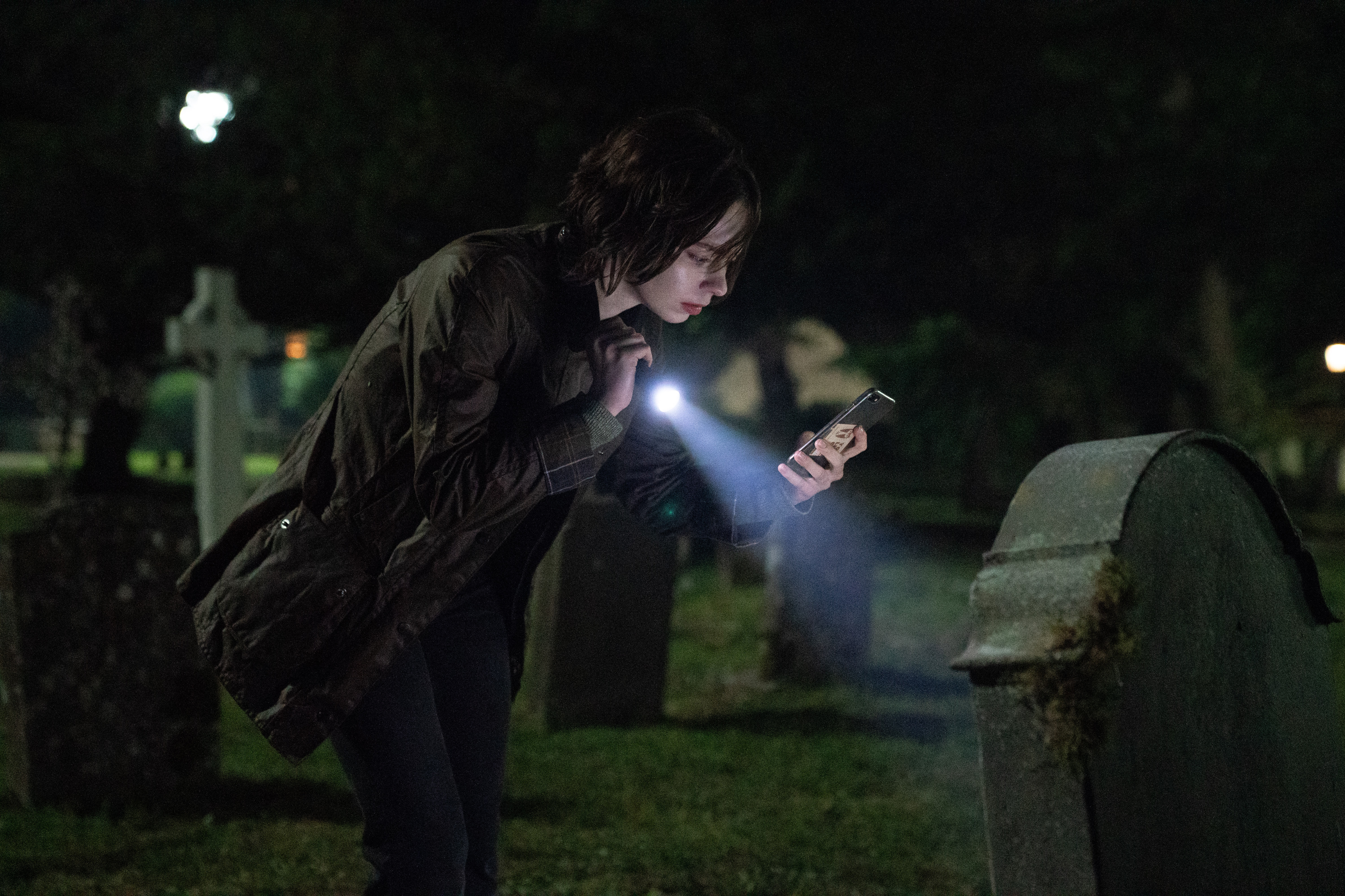 Emma Myers as Pip Fitz-Amobi shining a flashlight on a grave in a cemetery in A Good Girl's Guide to Murder: Season 2