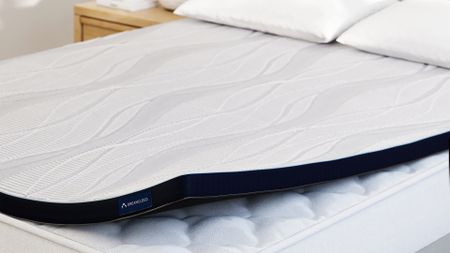 The DreamCloud Softer Topper on a mattress, with a corner lifted to show the mattress beneath