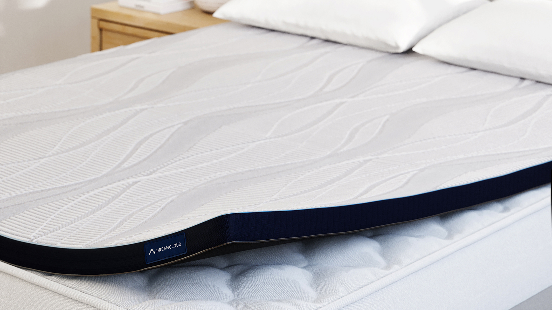 The DreamCloud Softer Topper on a mattress, with a corner lifted to show the mattress beneath