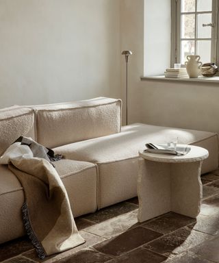 Cozy block sofa upholstered in boucle fabric, sculptural, raw stone side table, stone flooring