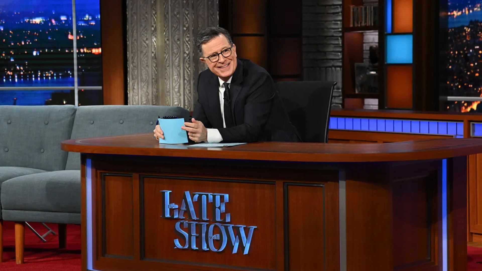 Stephen Colbert at his Late Show desk, holding blue cards