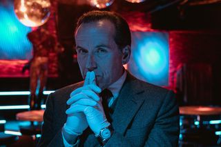 Professor T season 2: Ben Miller as Professor Jasper Tempest, standing in dim light on what looks like a nightclub dancefloor, with plastic gloves on his hands, which are clasped and his index fingers are pressed against his lips