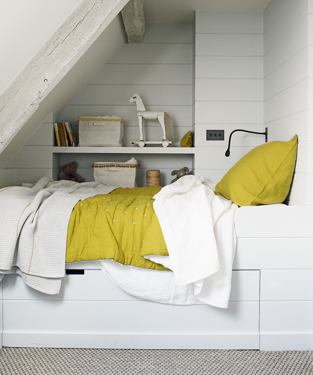 Small bedroom ideas for kids illustrated by a built-in alcove bed painted white with shelving and yellow bedlinen.