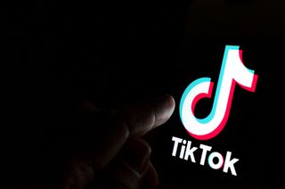 A finger about to press the TikTok logo in the dark