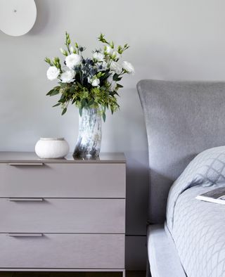 neutral bedroom with gray headboard, gray bedside cabinet and white statement wall light