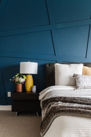 blue bedroom with modern paneling, brown bed, brown side table, yellow lamp, neutral bedding