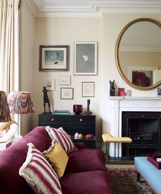Elegant living room with fireplace, oval mirror mounted above, plum sofa, framed pictures on the wall.
