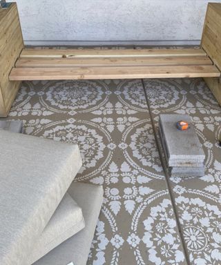 Wooden outdoor sofa frame on brown and white decorative patio tiles, taupe cushions in foreground