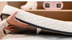 Hands holding a mattress topper over a bed