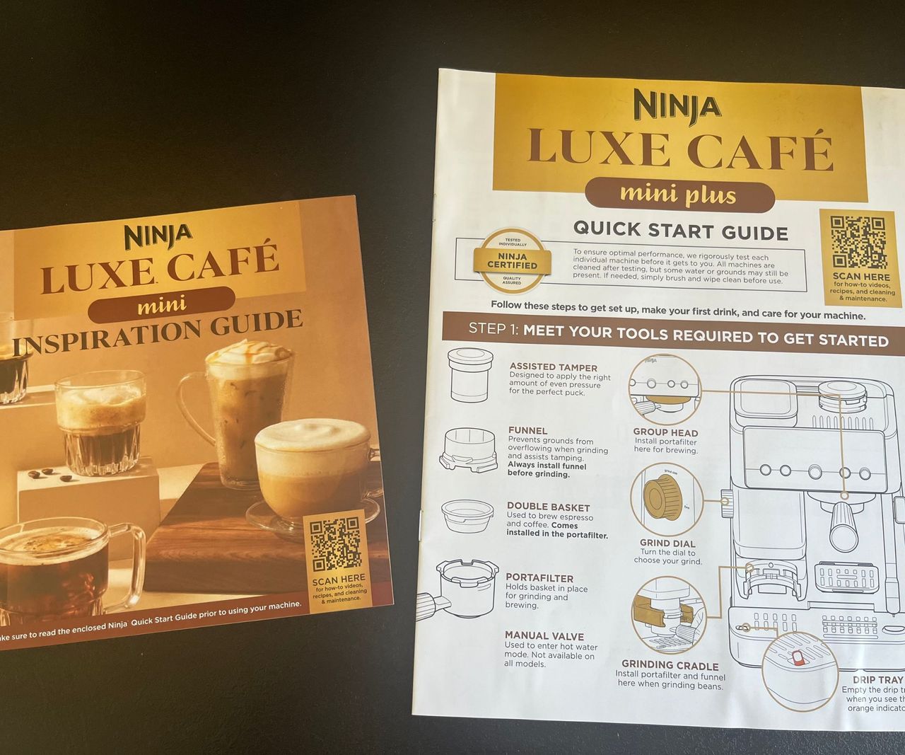 Two white and gold instruction manuals for the Ninja Luxe Caf&eacute; on a black kitchen counter
