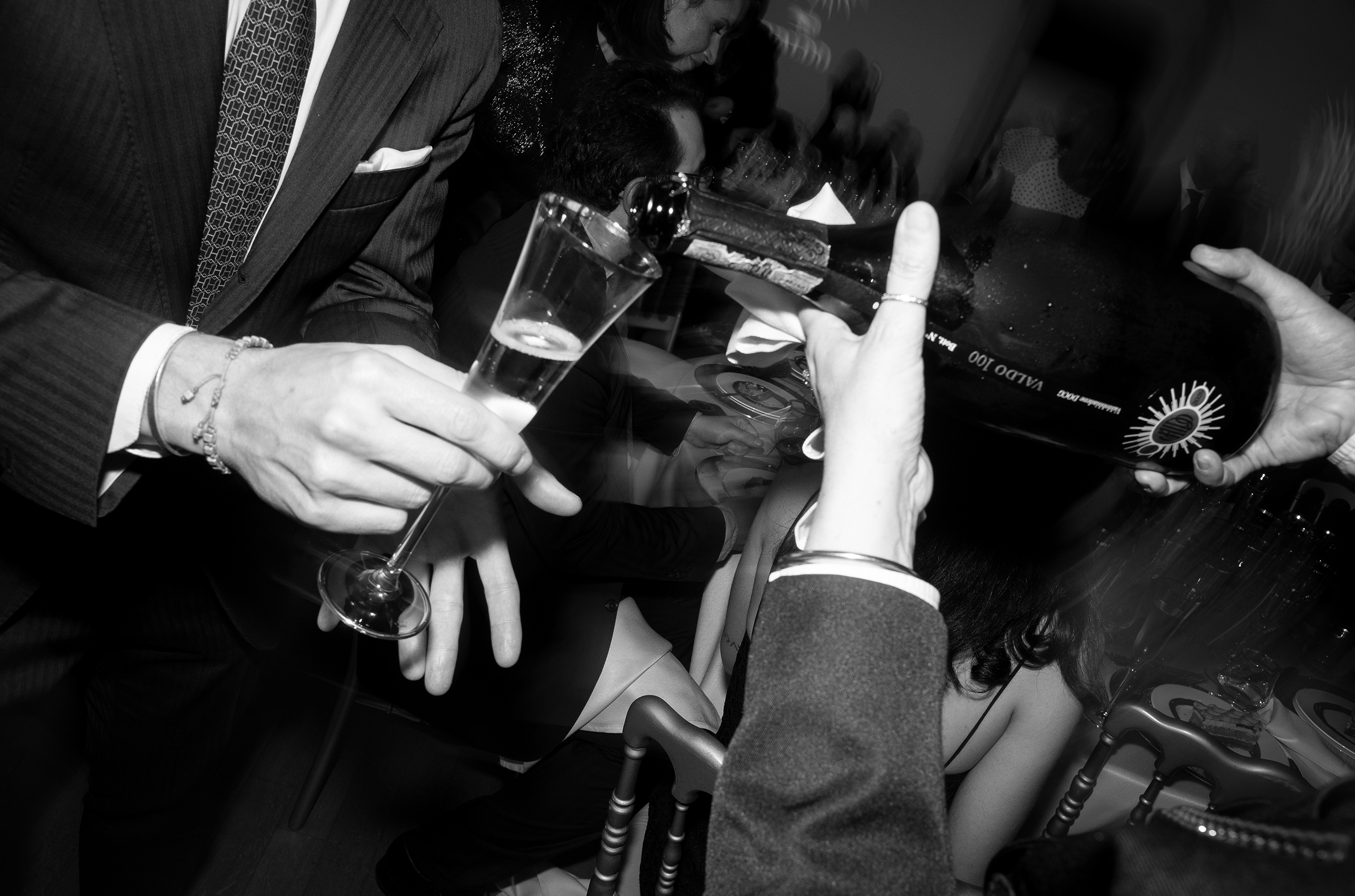 Black and white photo of a hand pouring a glass of Prosecco into a flute glass