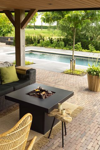Faux fire pit logs on a patio area beside a pool with rattan garden furniture