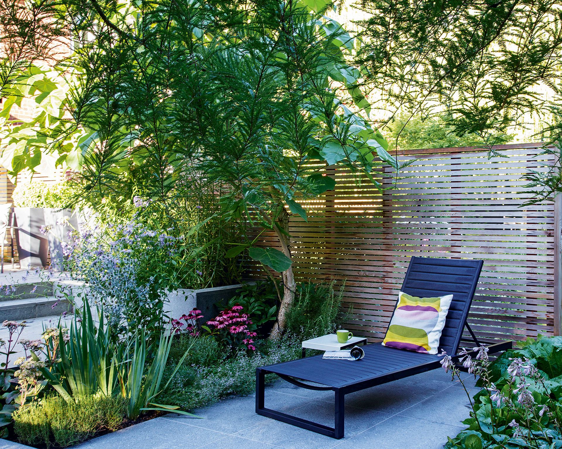 A garden patio area with a wooden fence and a black sun lounger