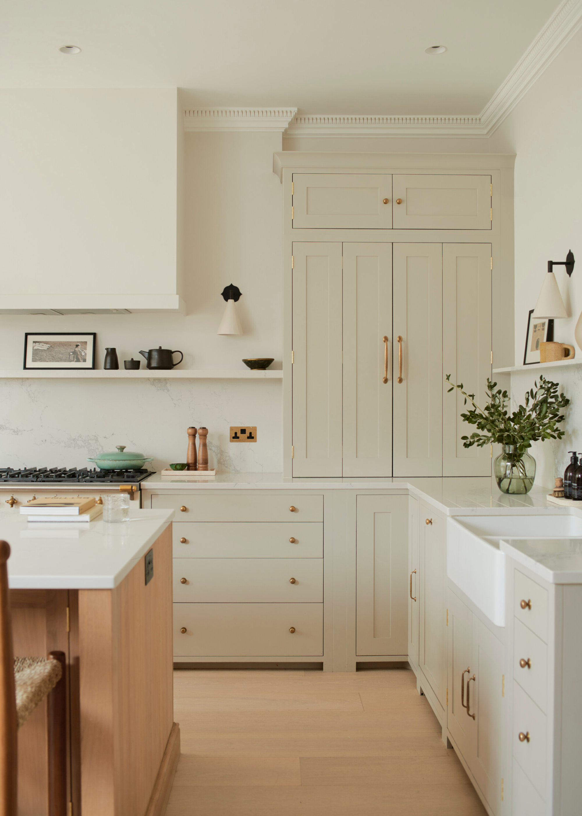 A light off white kitchen with high ceiling and architectural moldings, a kitchen island and a boxed in custom extractor above the cooker