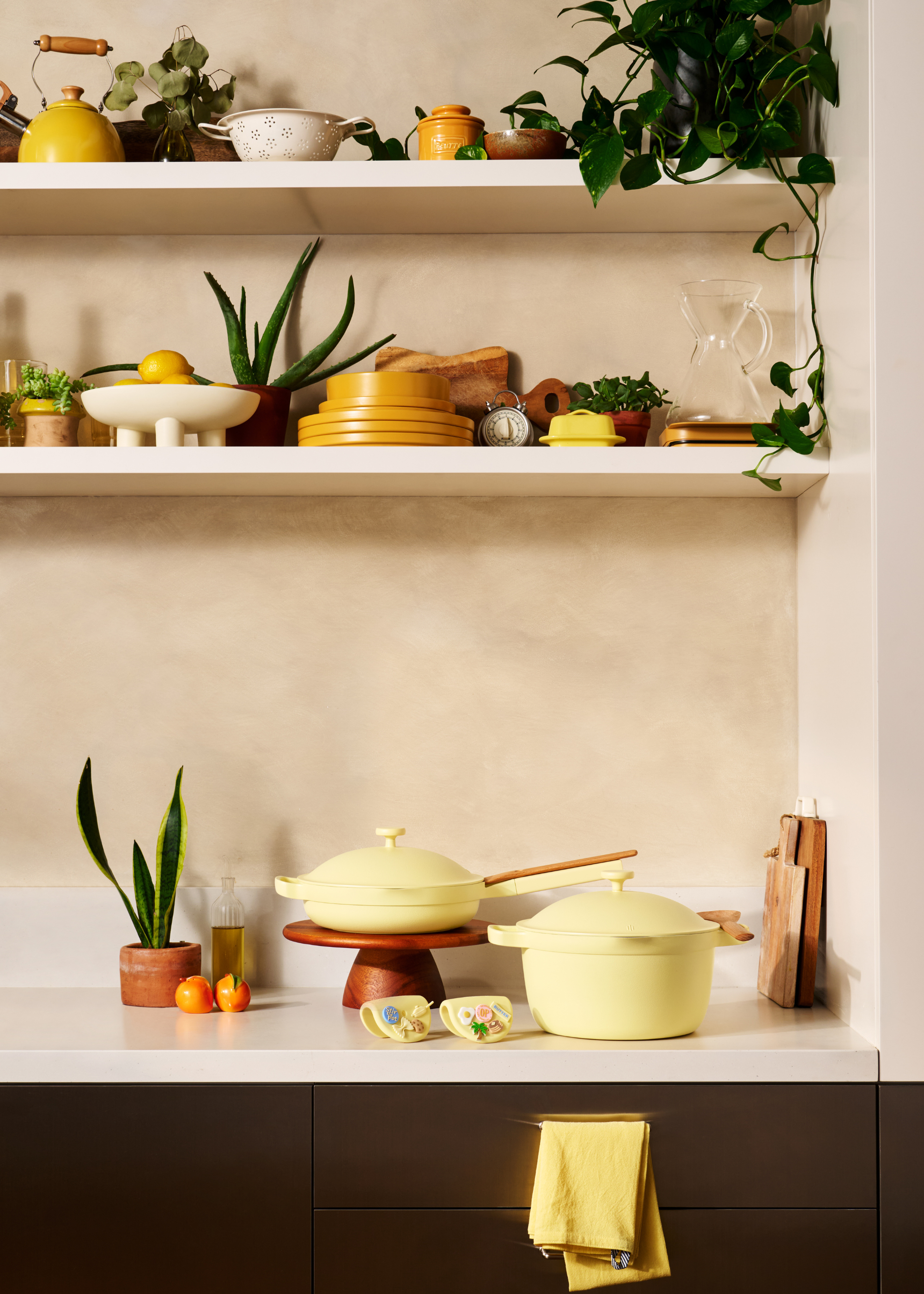 A set of butter yellow cookware on a counter by a limestone backsplash