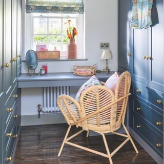 White dressing room with blue wardrobes on either side, and a dressing table with rattan chair in the middle