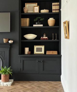 living room with one white wall and remainder of space, including built in alcove shelving and fireplace painted black