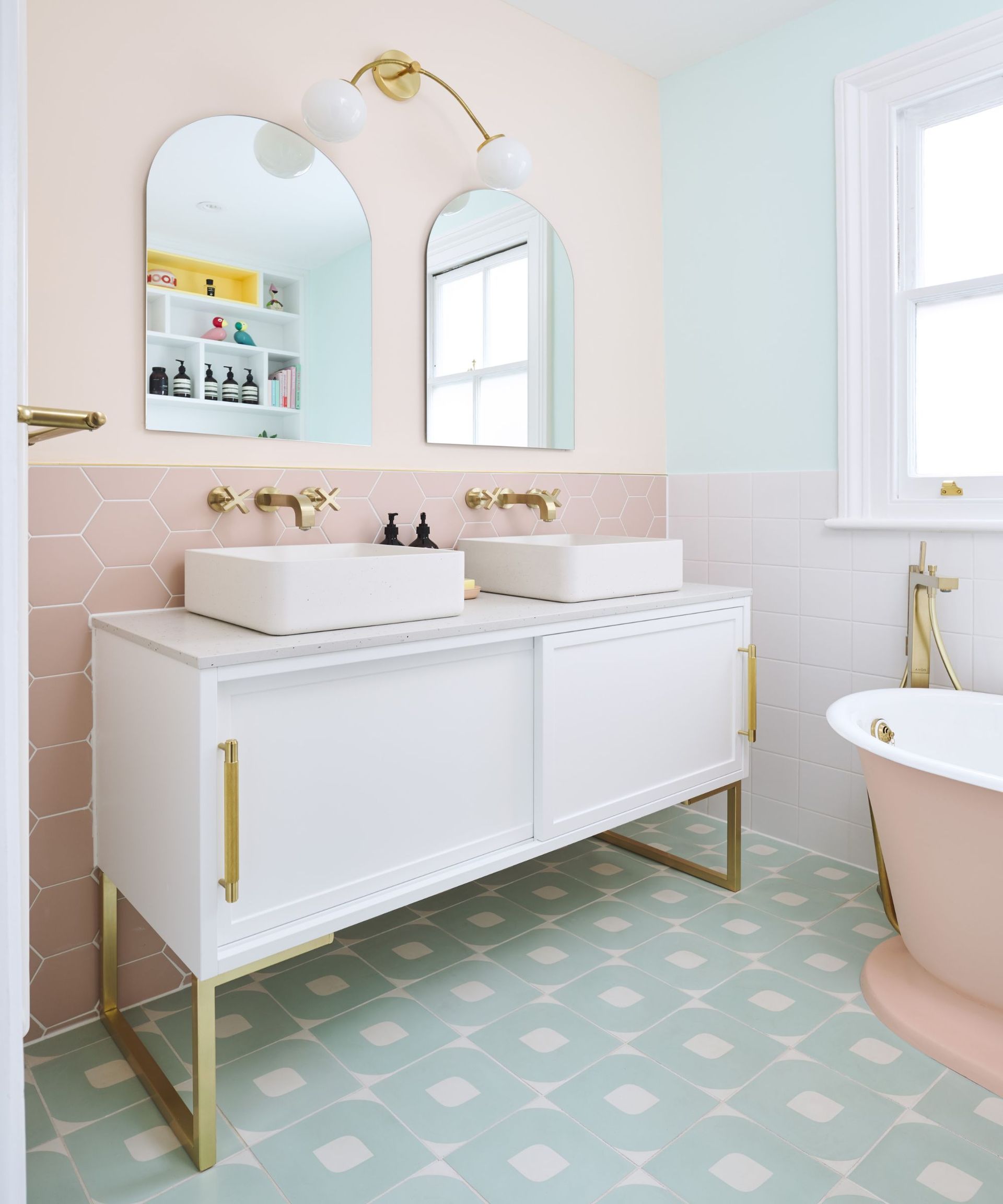 A mint green and light pink pastel bathroom with a matching pink bathtub and gold hardware