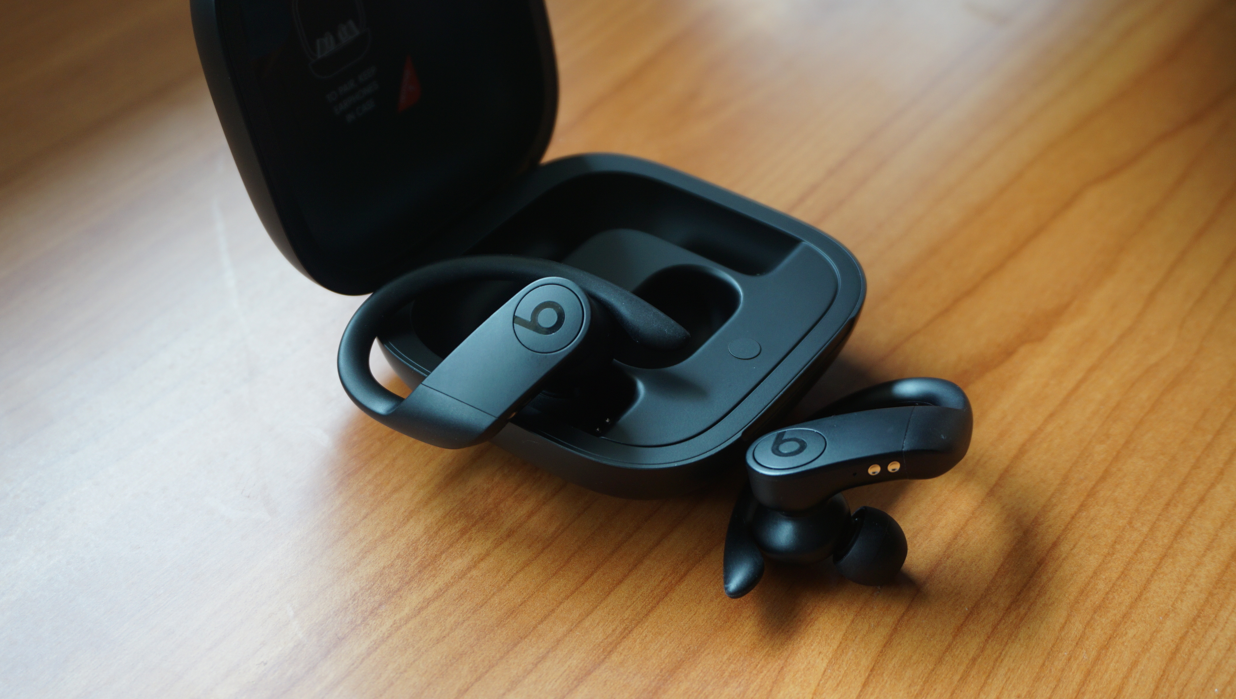 Beats Powerbeats pro headphones pictured next to their charging case on a wooden surface.