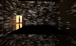 Black room with man standing in doorway on bottom left, walls covered in white words