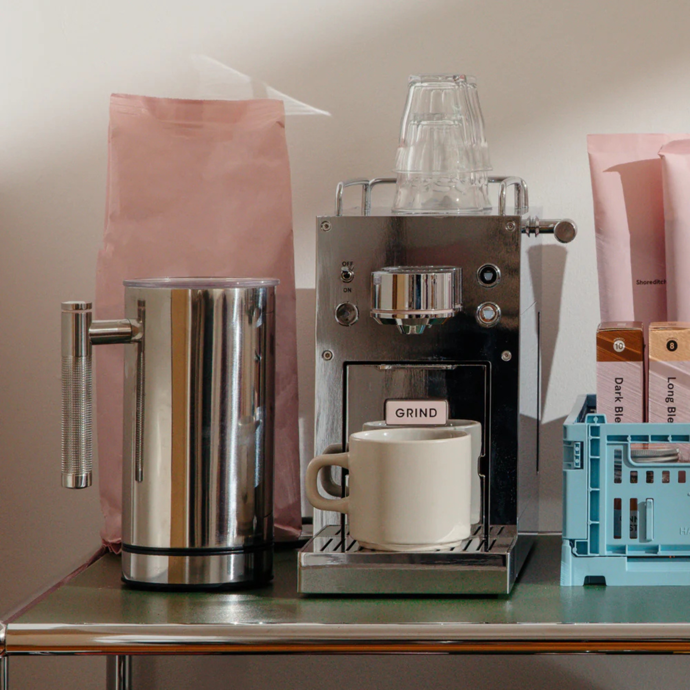 a silver pod coffee machine on a surface next to a milk frother