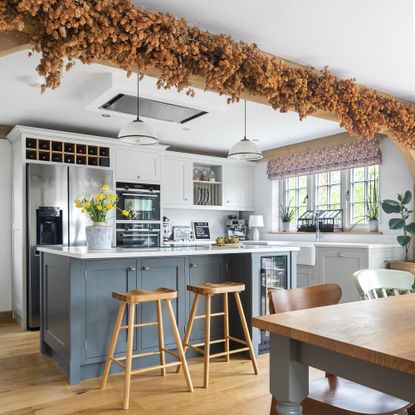 kitchen in oak frame house with blue island, large stainless steel fridge and dried hops on ceiling beam