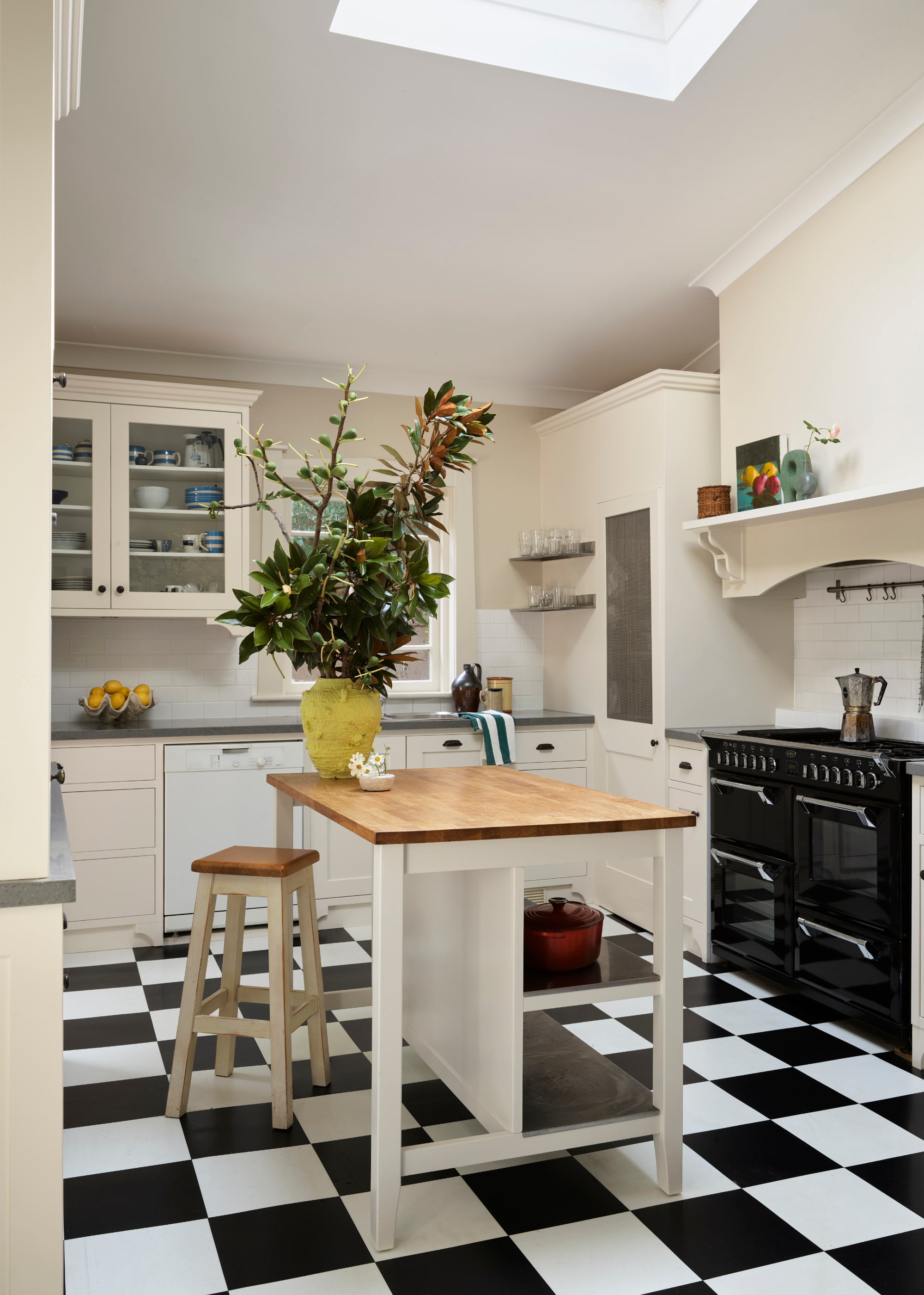 A small kitchen with checkerboard floors, a black oven and stove unit, a small island and a stool