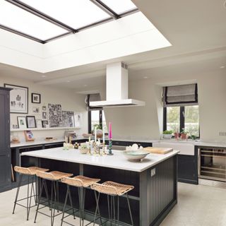 Kitchen with oversized islands with floating extractor fan and stools beneath skylights