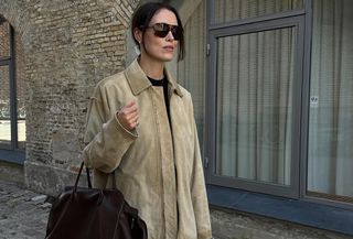 Annabel wears a tan suede jacket, oversize sunglasses, a brown leather bag, and black capri pants.