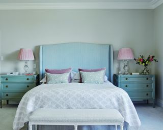 pastel bedroom with bed with oversized, winged headboard, aqua bedside chests and end of bench bed