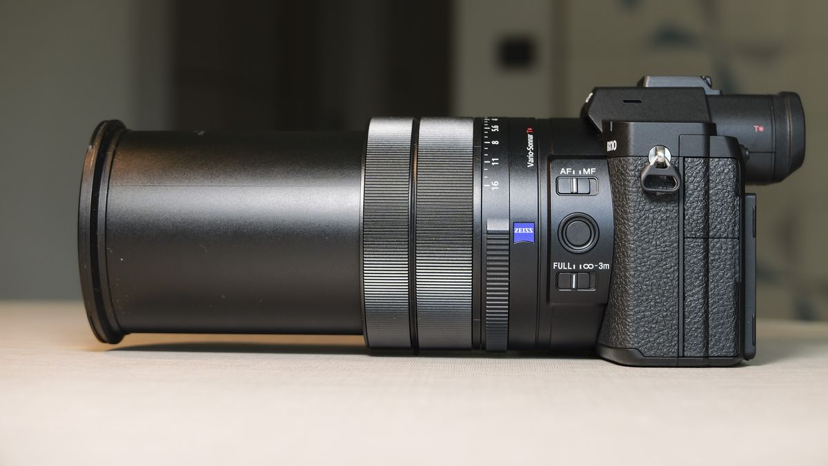 The side profile of the Sony RX10 V bridge camera, on a white table with a patterned wallpaper background, its lens is fully extended