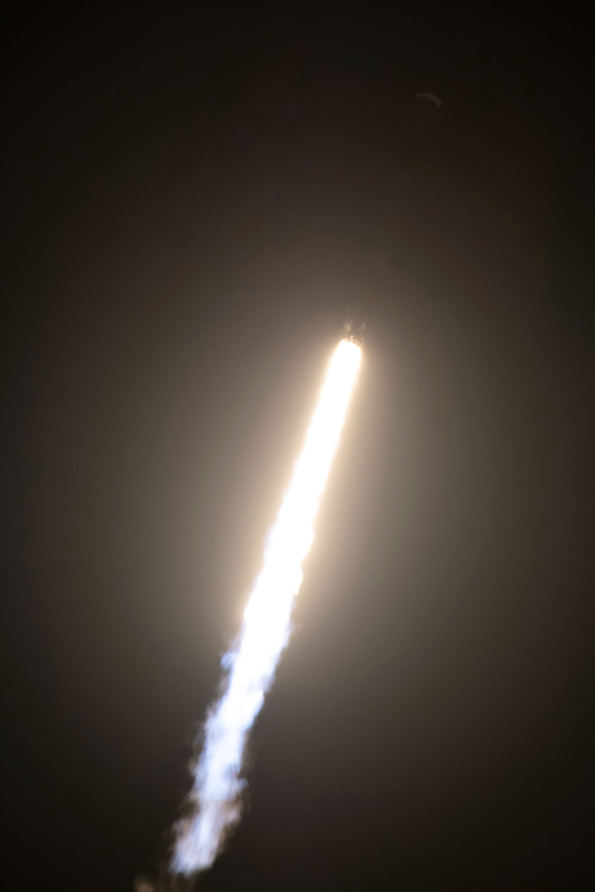 A white and black rocket lifts off into the night sky, with only its bright whiite thrust visible