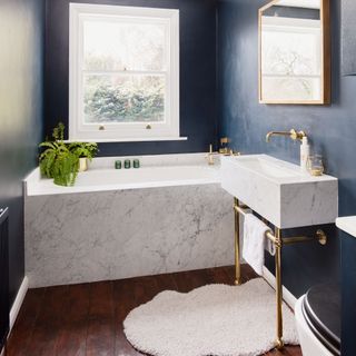 bathroom with navy blue walls and wooden floor and bathtub and washbasin with towel and white rug