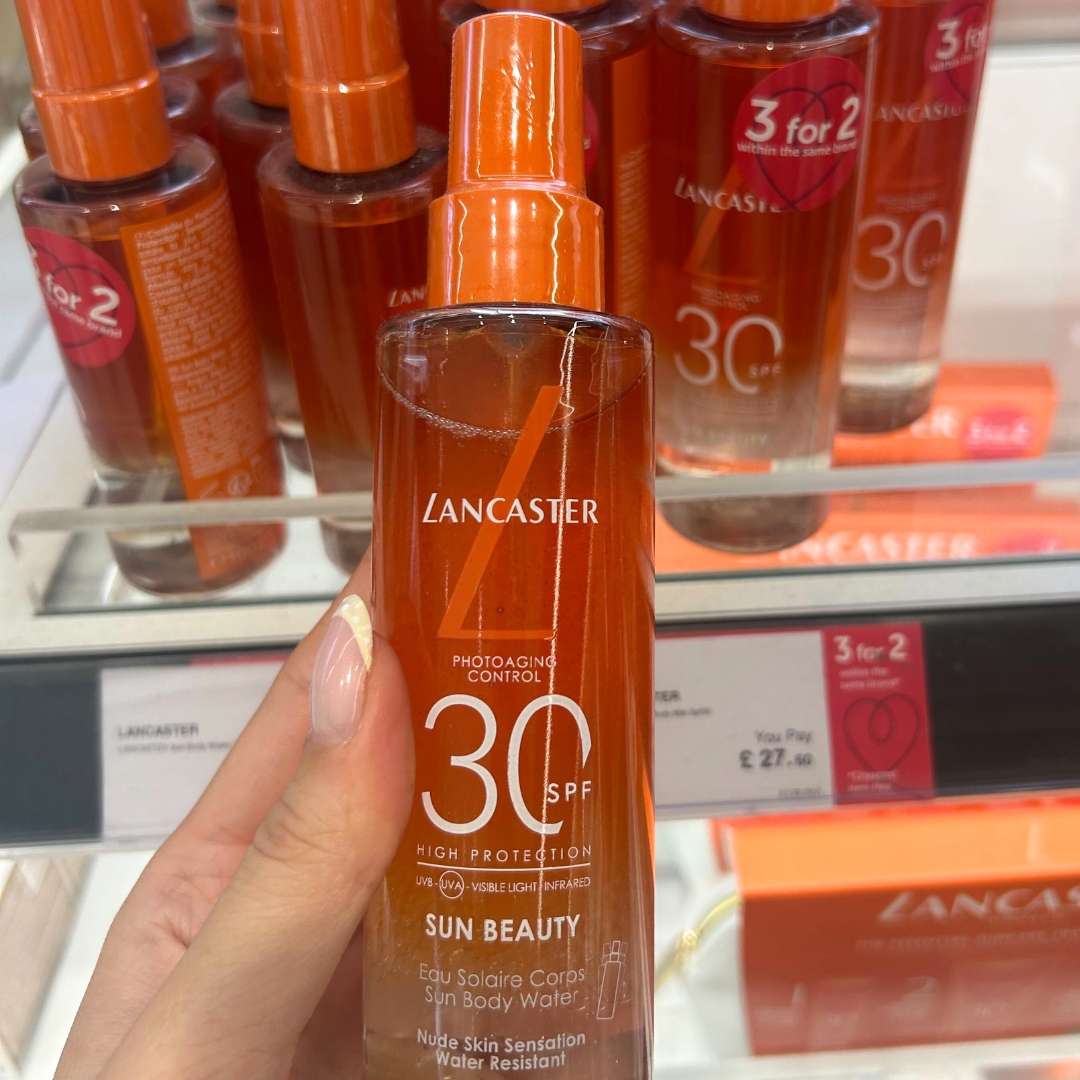 Hand holding bottle of Lancaster Sun Beauty Body Water SPF30 100ml in World Duty Free