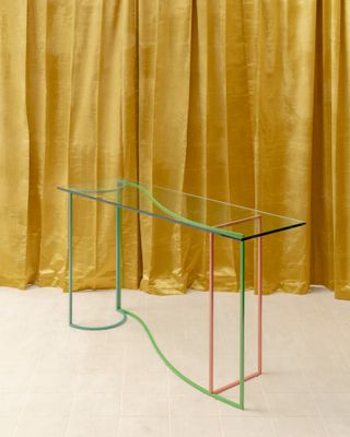 Glass and metal console table by Sight Unseen in front of a gold curtain