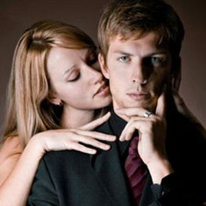 man in suit with woman behind him nuzzling his neck