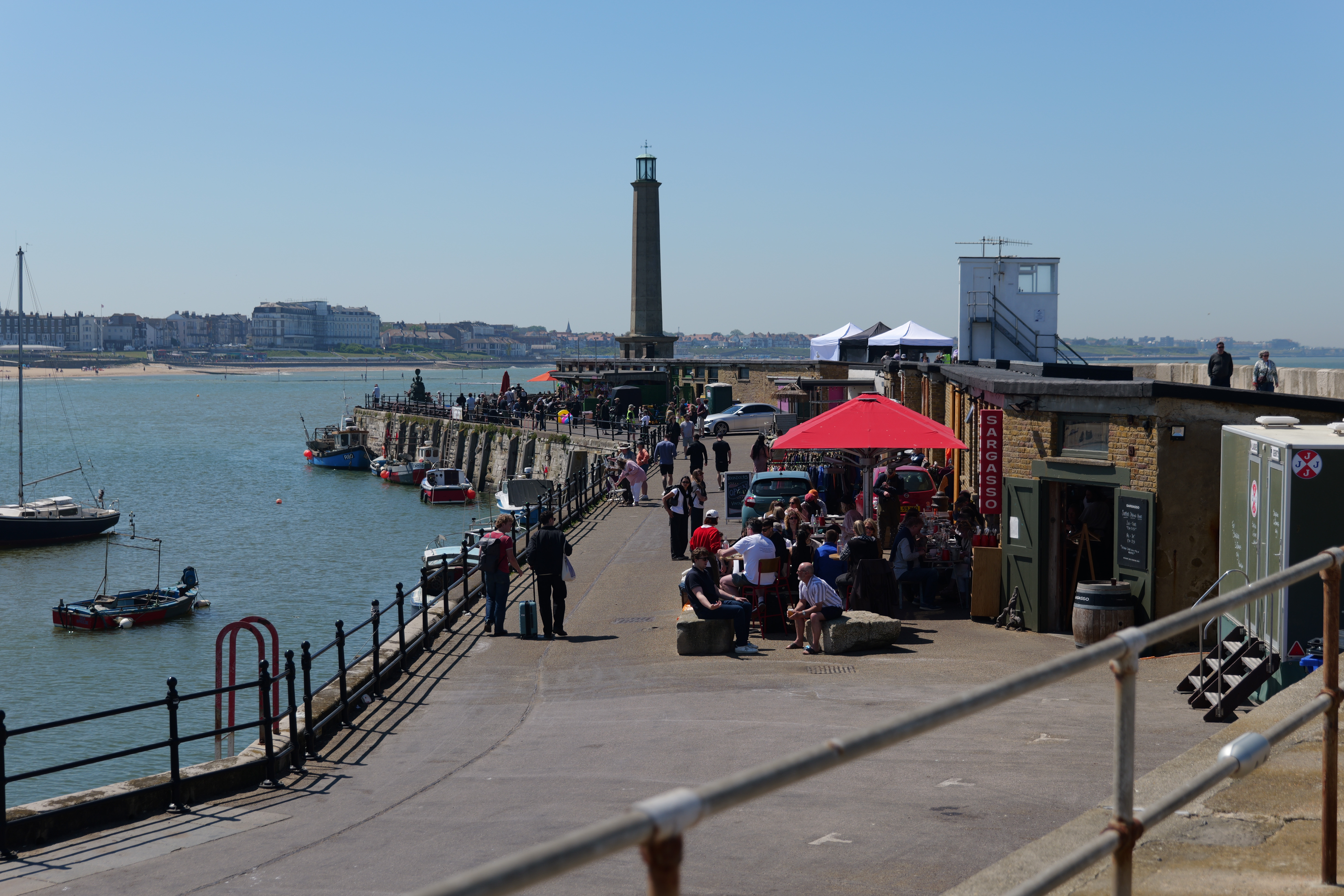 A pier with lots of people and a lighthouse at the end
