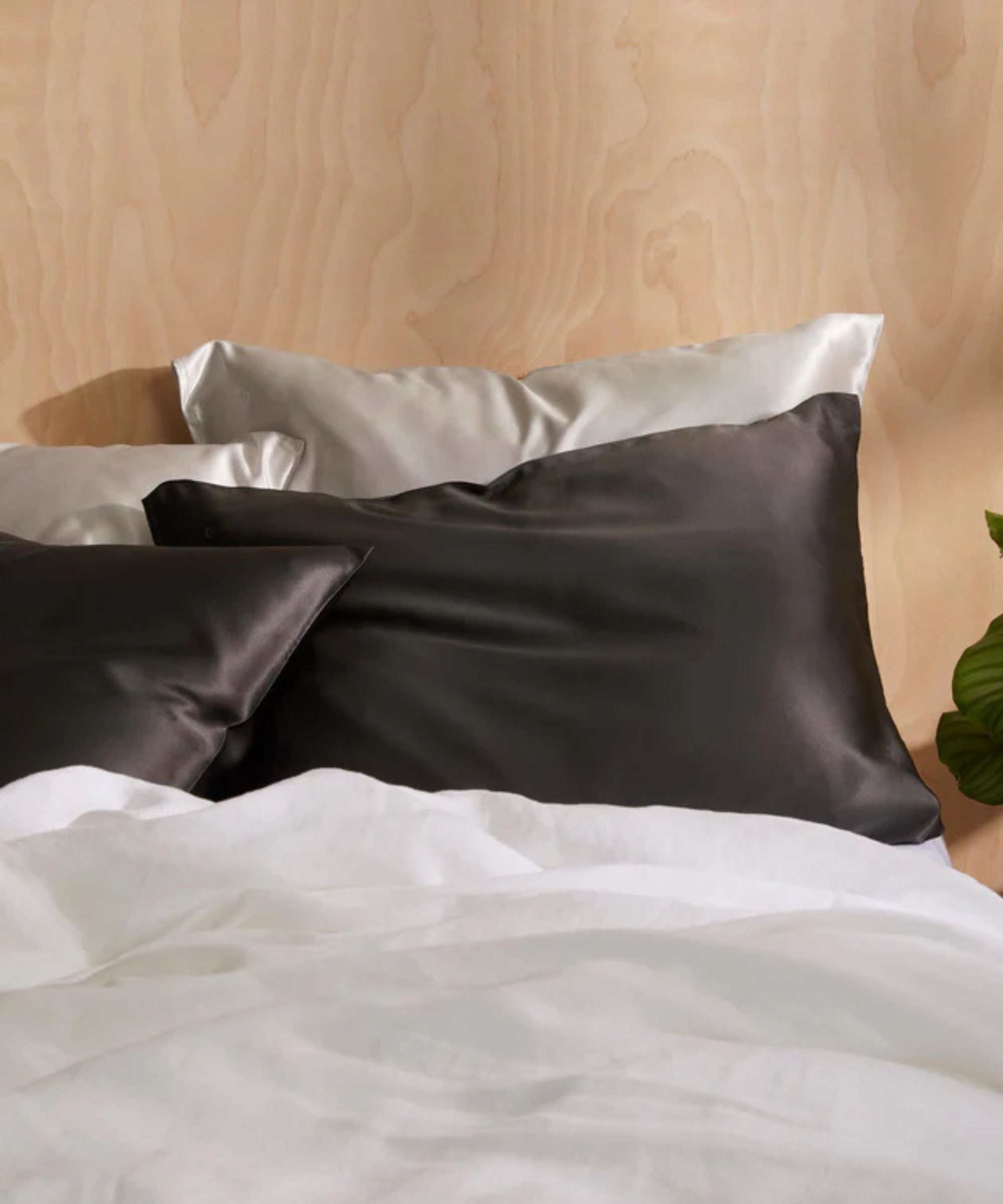 Pale oak bedframe with white sheets, two white silk pillowcases, and two grey silk pillowcases in front