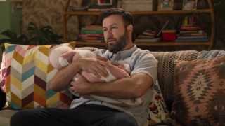 Ludo holding baby on couch in High Potential