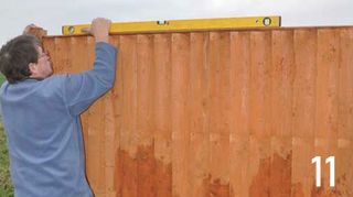 Man holding yellow spirit level on top of fence panel