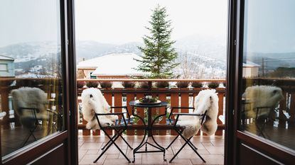 Winter balcony with coffee table, cozy chairs covered with white fur and splendid snow-covered mountains view.